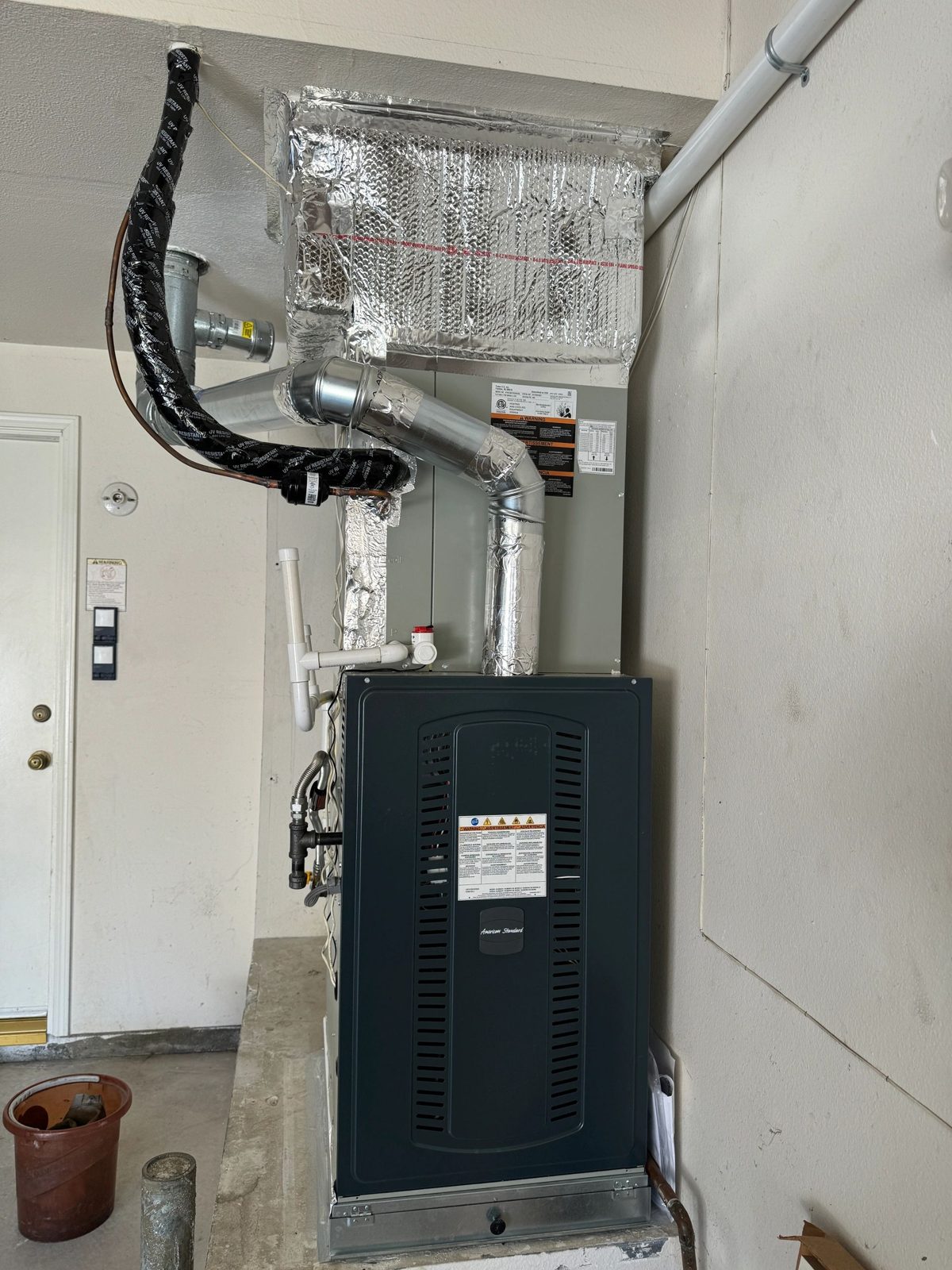 American Standard furnace with ducts, pipes, and insulation in utility area
