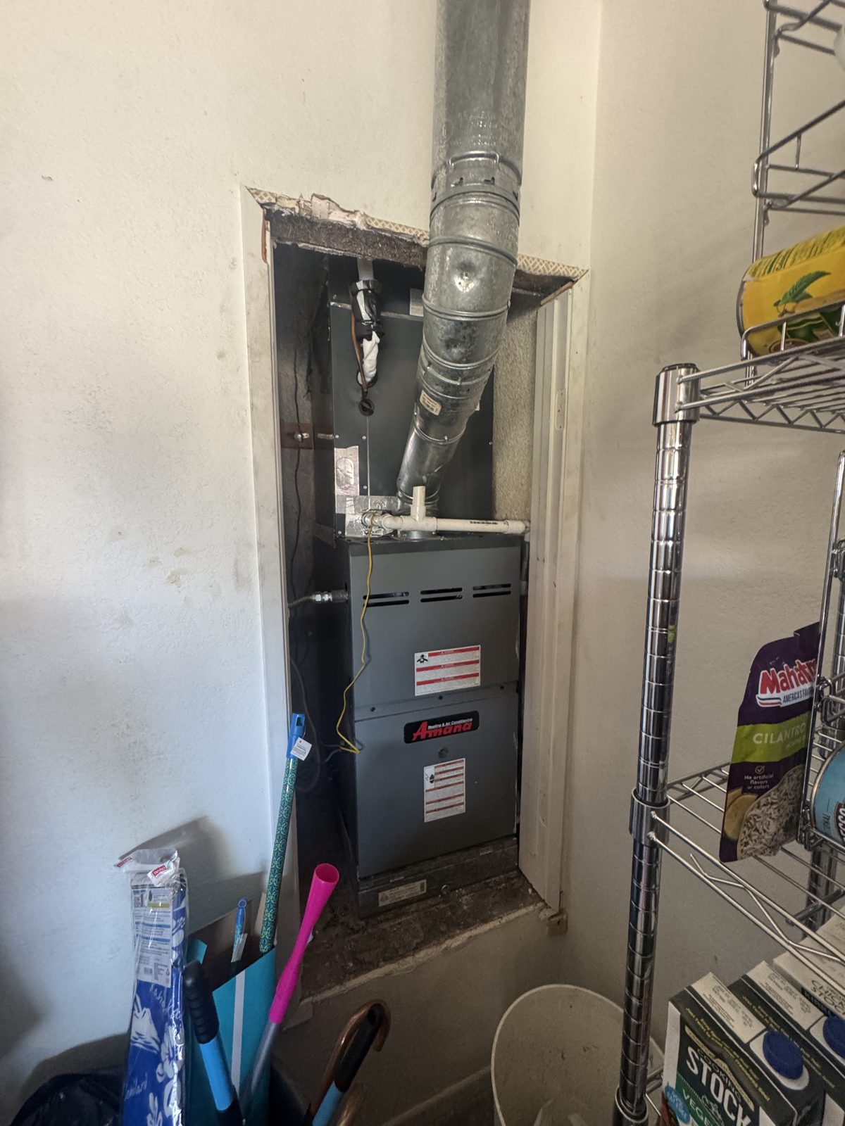 Old furnace in closet with vent pipe and gloved hand holding damaged foam insulation on pipes