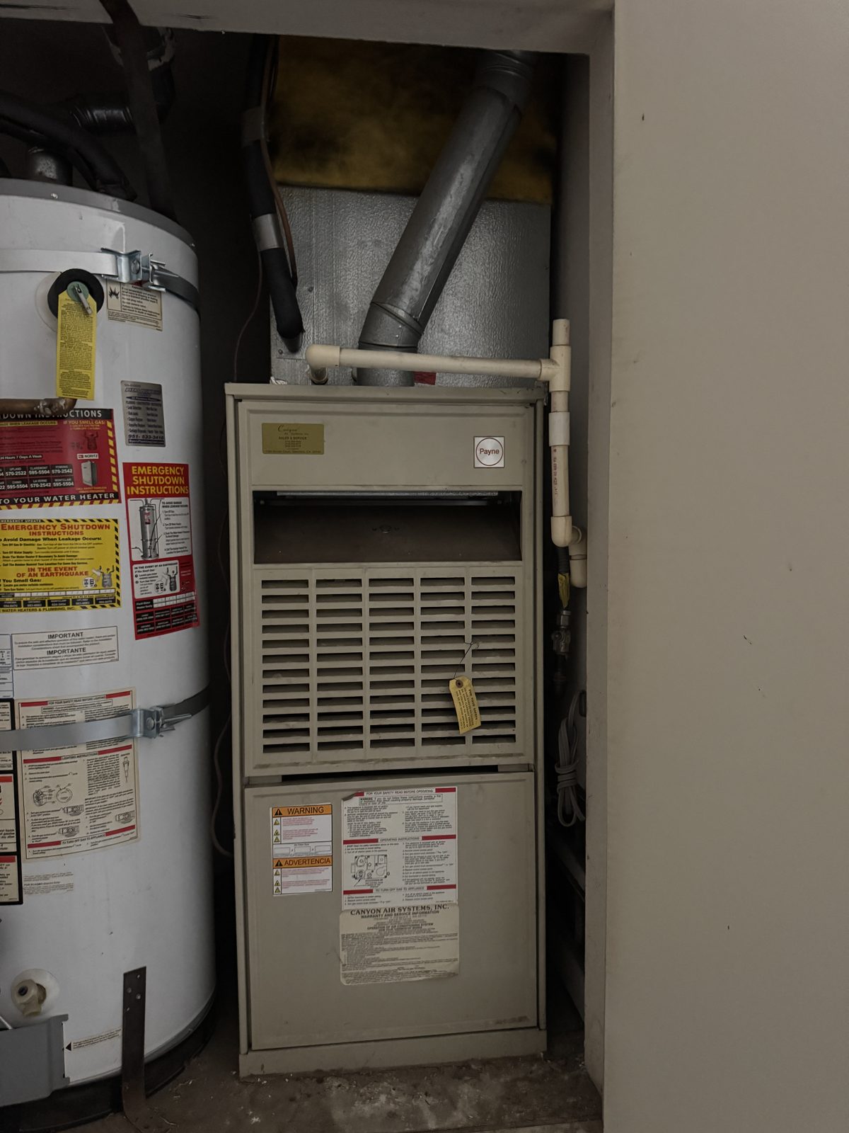 Old furnace and water heater in Chino Hills utility closet with two outdoor AC units beside building before repair service