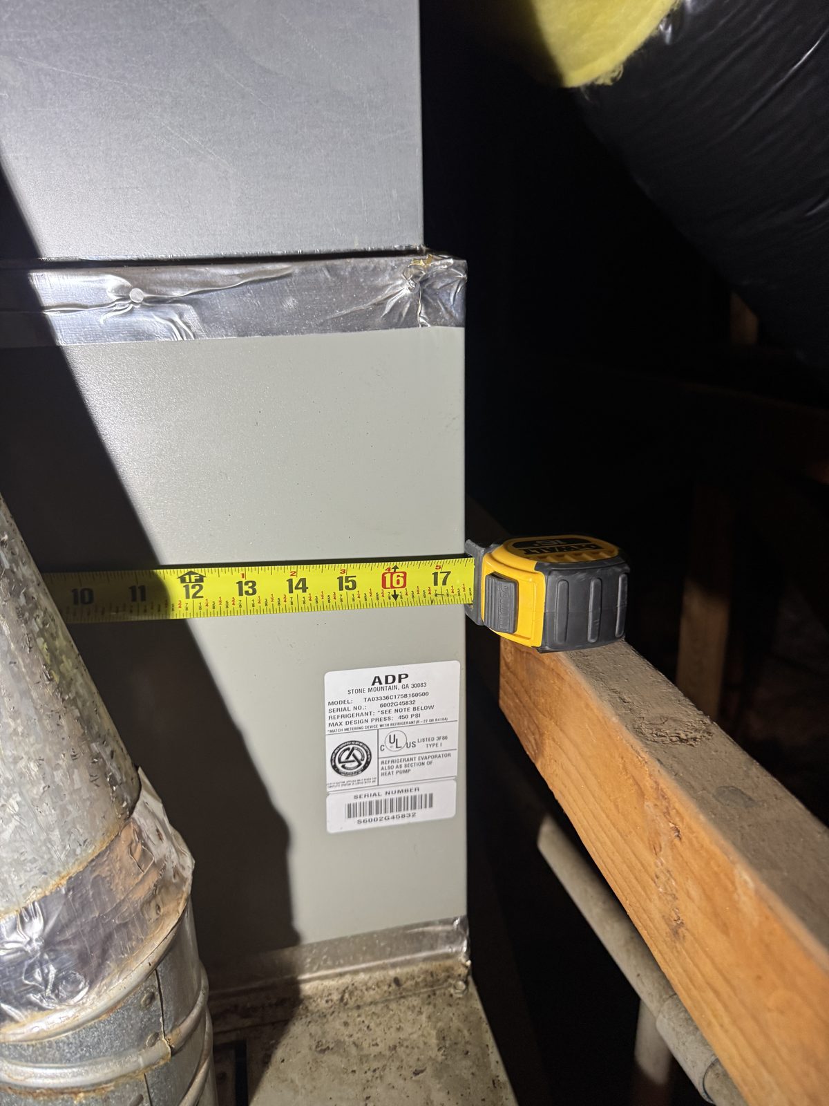 HVAC duct with tape measure and ADP label next to attic furnace with ducts and pipes