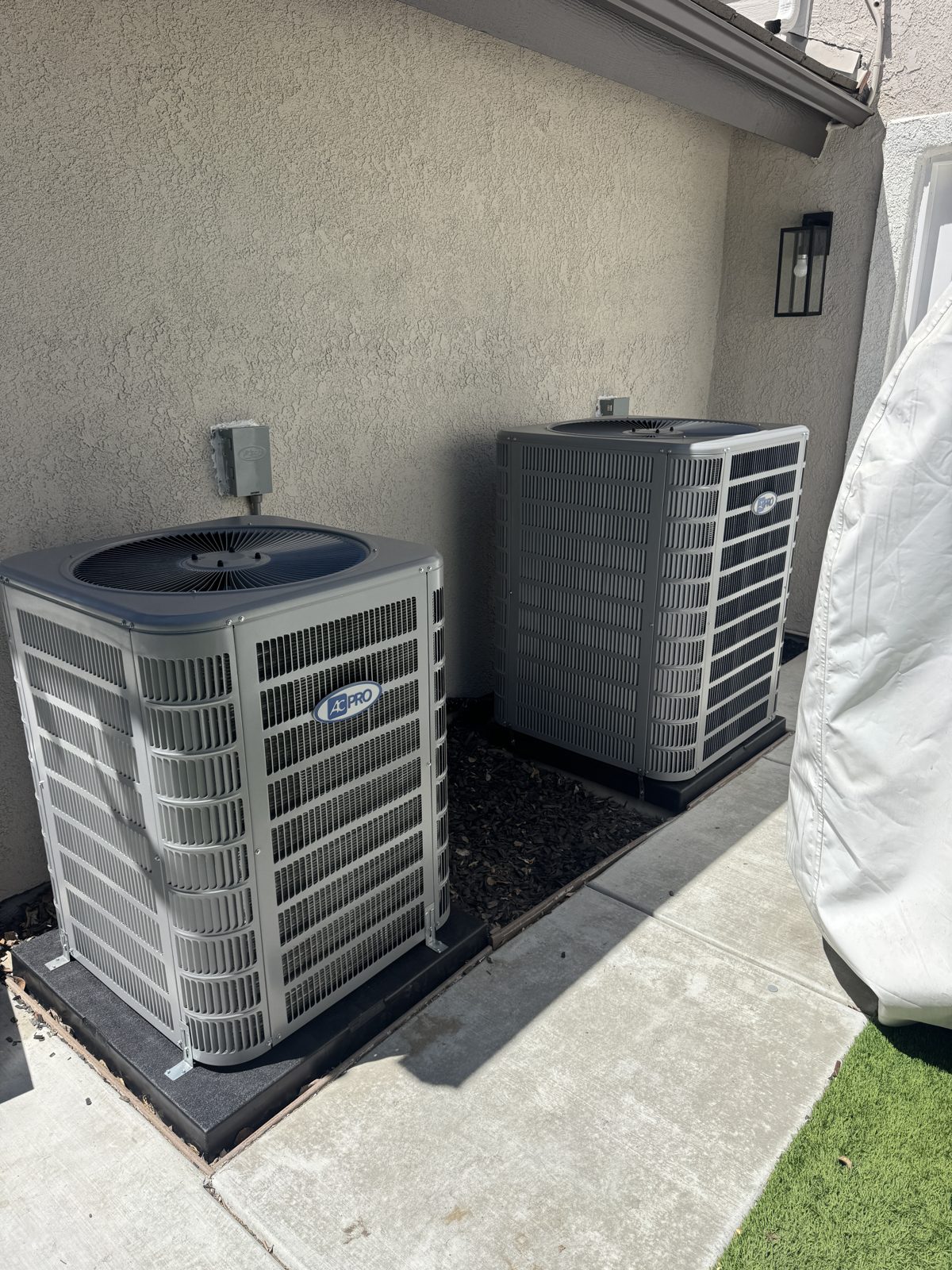 Two outdoor HVAC condenser units by building wall with furnace and water heater setup in Chino Hills