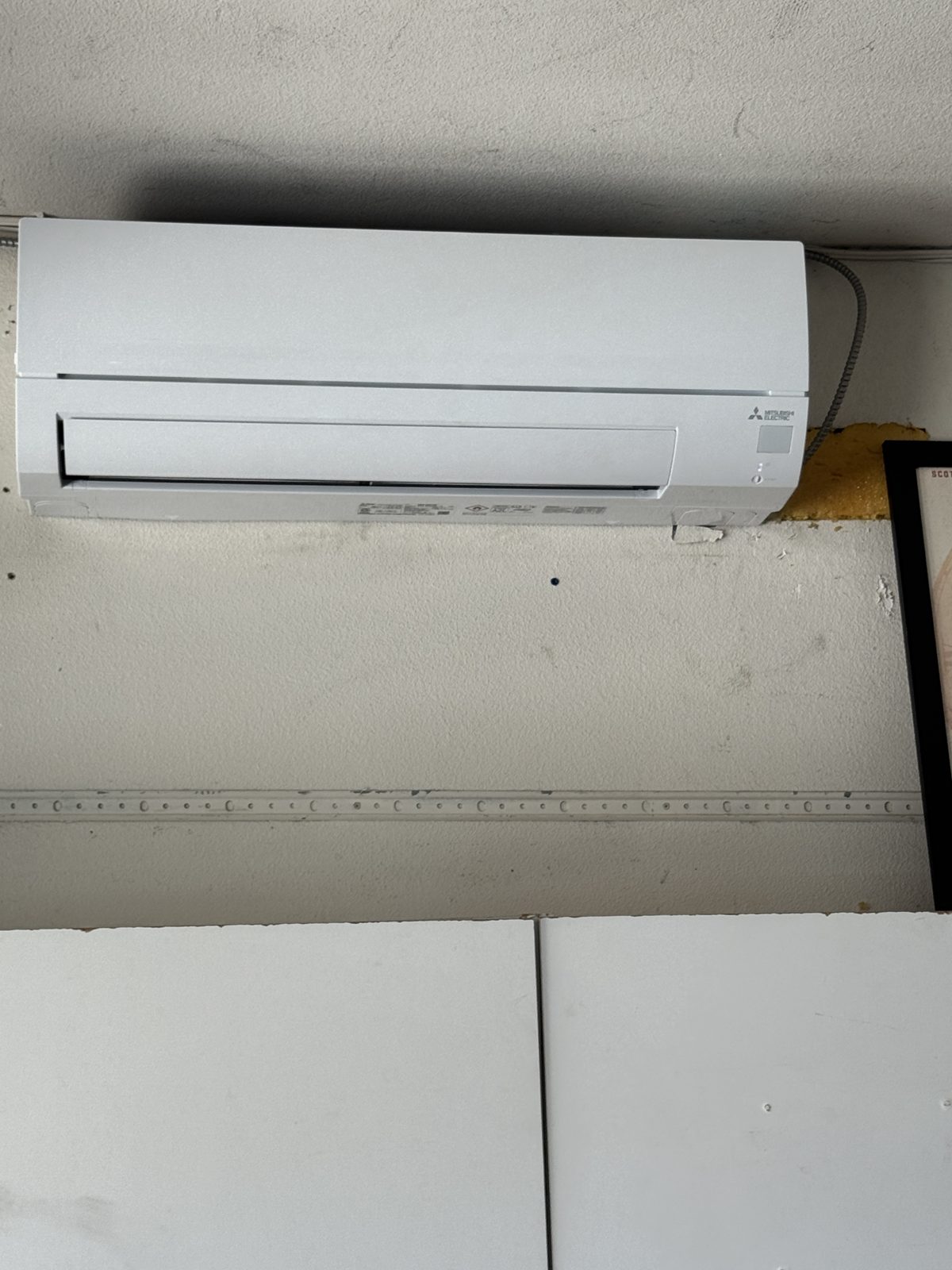 White Mitsubishi air conditioner mounted on wall above cabinets with movie poster