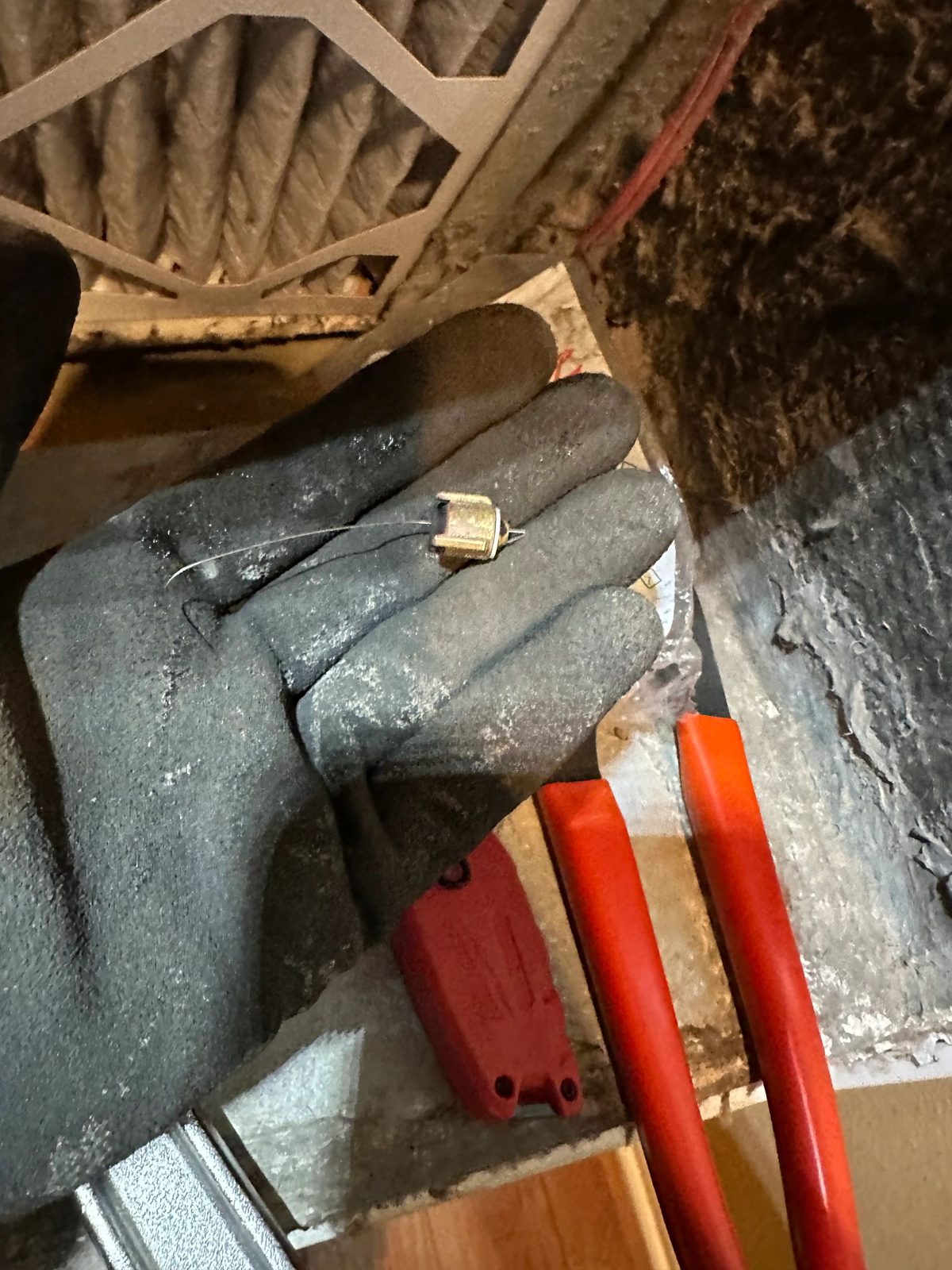Gloved hand holding small brass component with thin wire